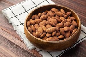 almendras en cuenco de madera sobre la mesa, merienda saludable, comida vegetariana foto