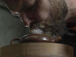 man with a beard breathes smoke into a traditional teapot photo