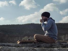 man with a beard drinks tea from a bowl on a background of mountains photo