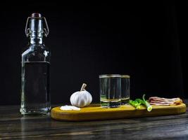 Botella de vodka, dos vasos de vodka frío sobre una tabla de madera foto