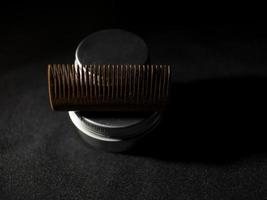 Peine de madera y frascos de cera para barba y bigote sobre un fondo negro foto