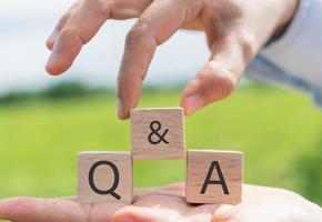 Q and A alphabet on wooden cube in hand hold with background photo