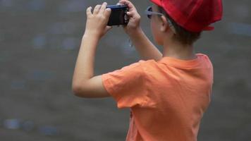 un garçon près d'un lac de montagne en train de prendre des photos.