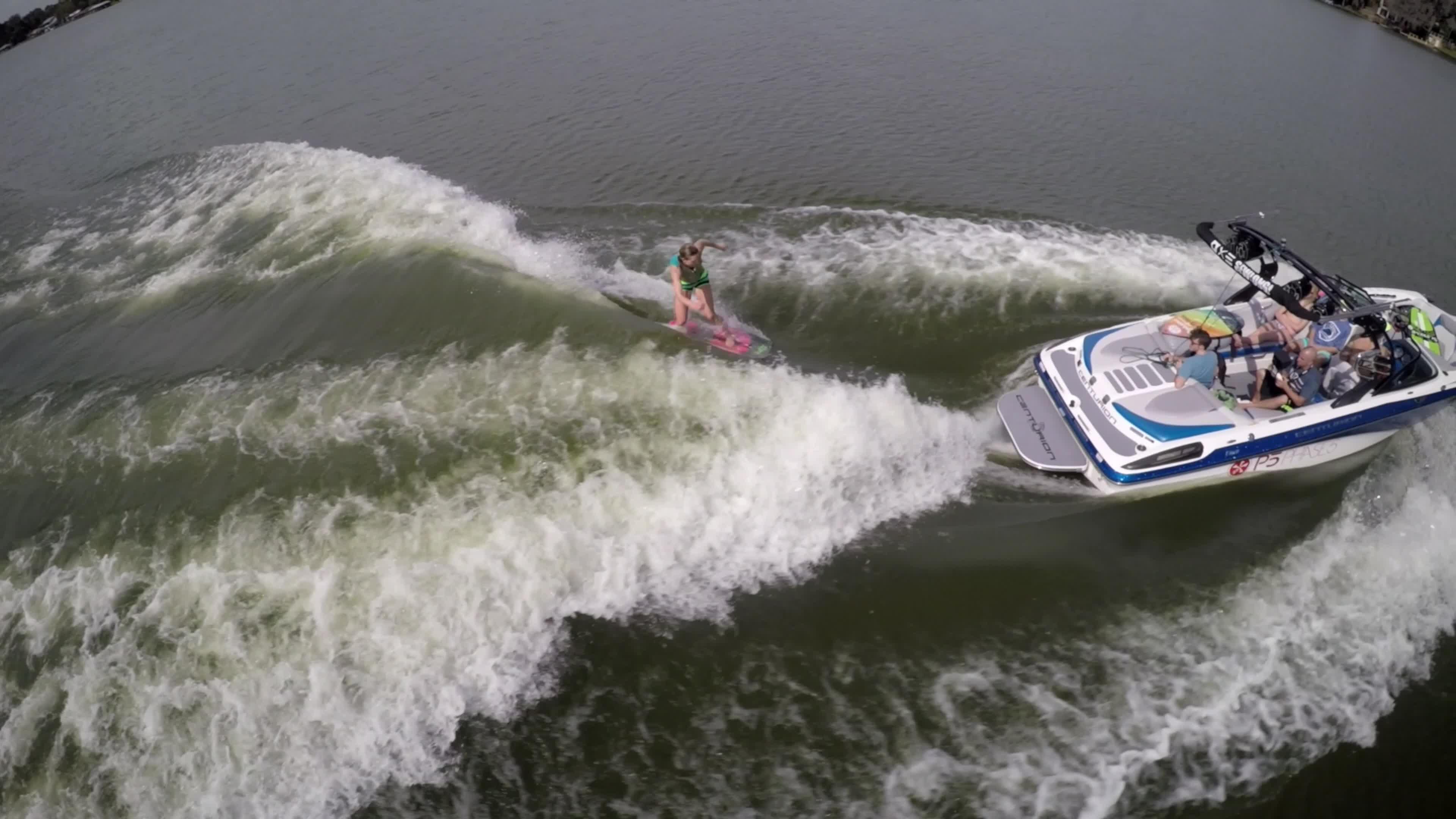 Aerial shot of a man wakeboard wake surfing behind a boat on a lake