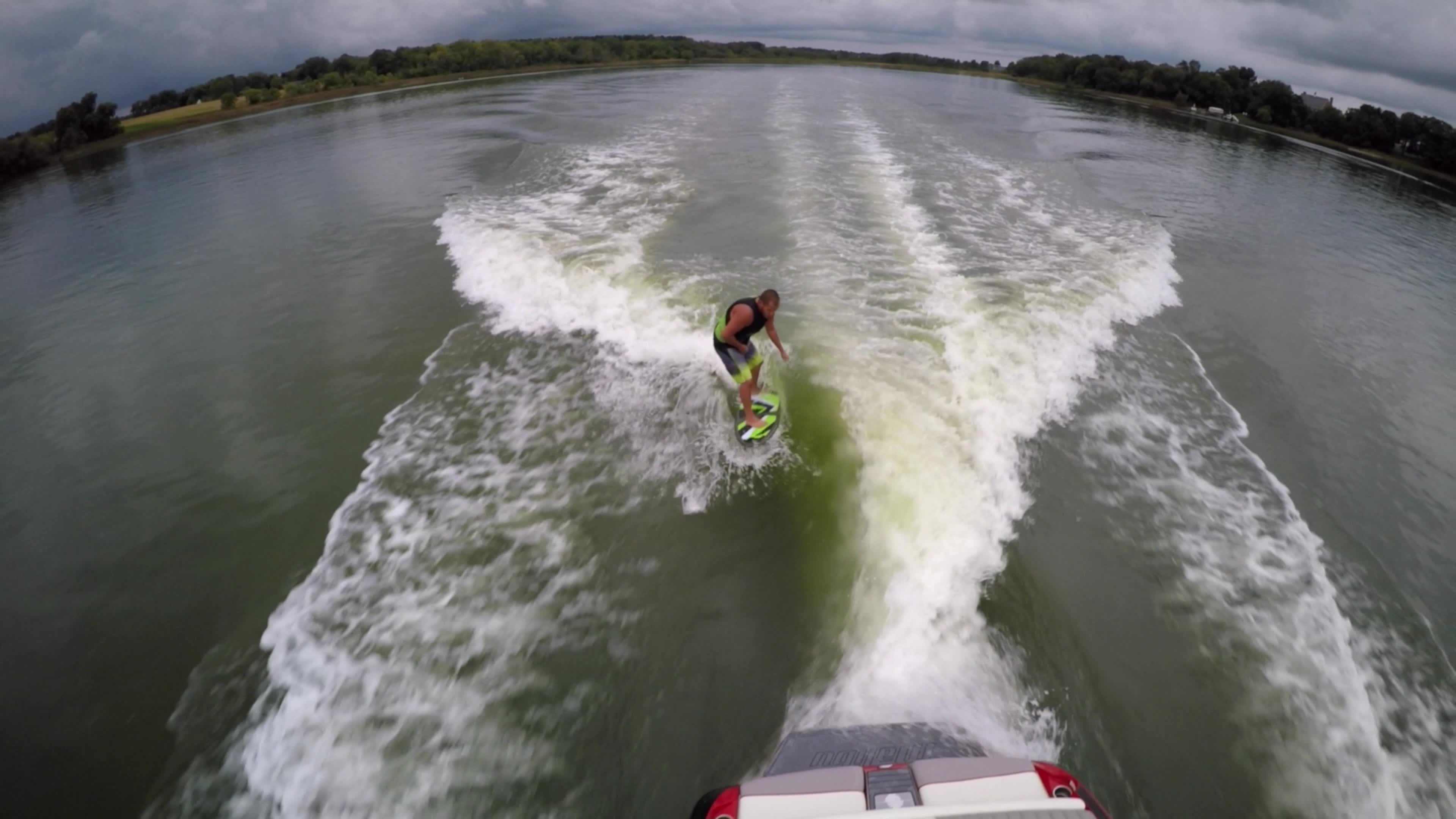 Aerial shot of a man wakeboard wake surfing behind a boat on a lake