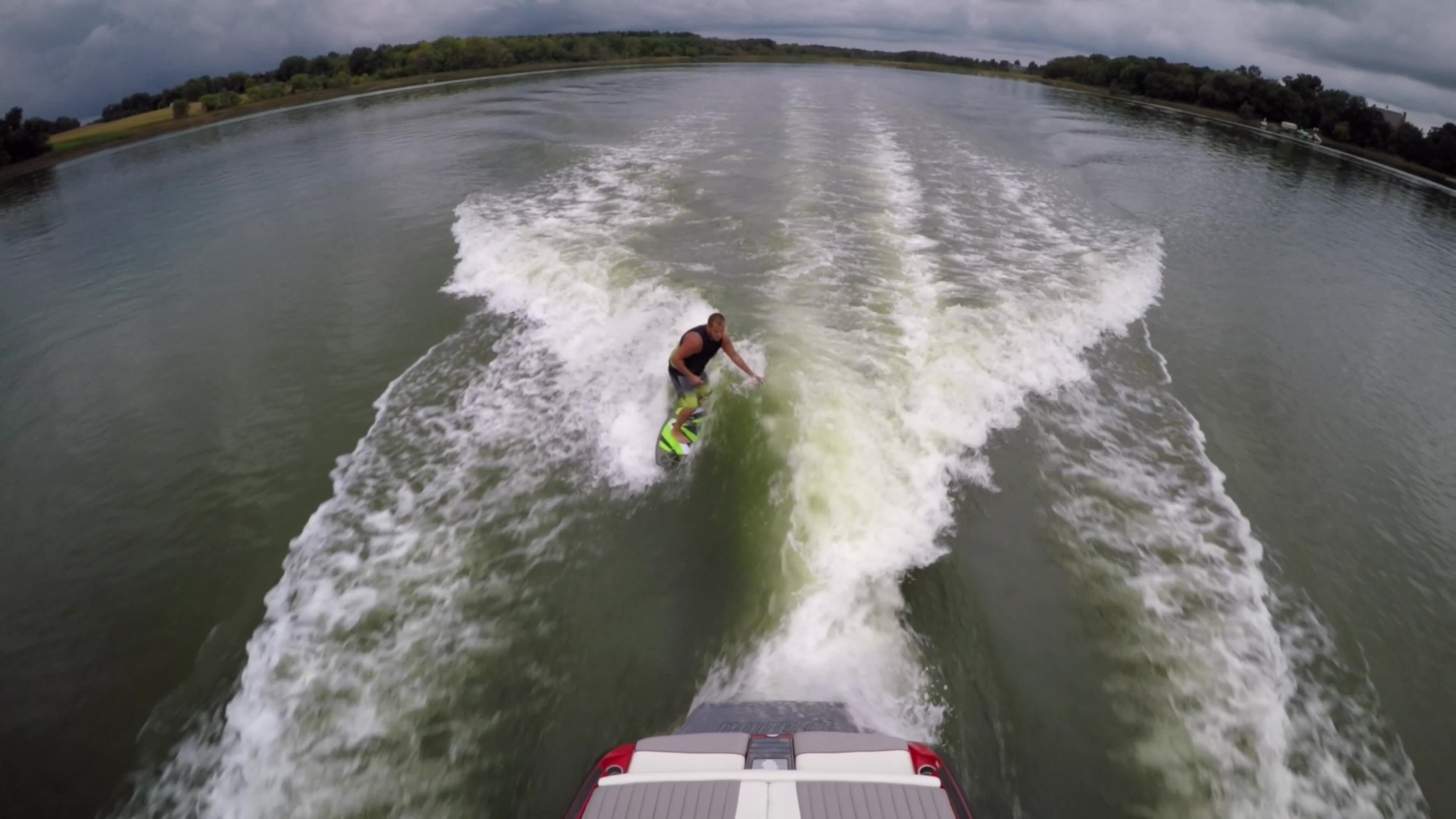 Aerial shot of a man wakeboard wake surfing behind a boat on a lake