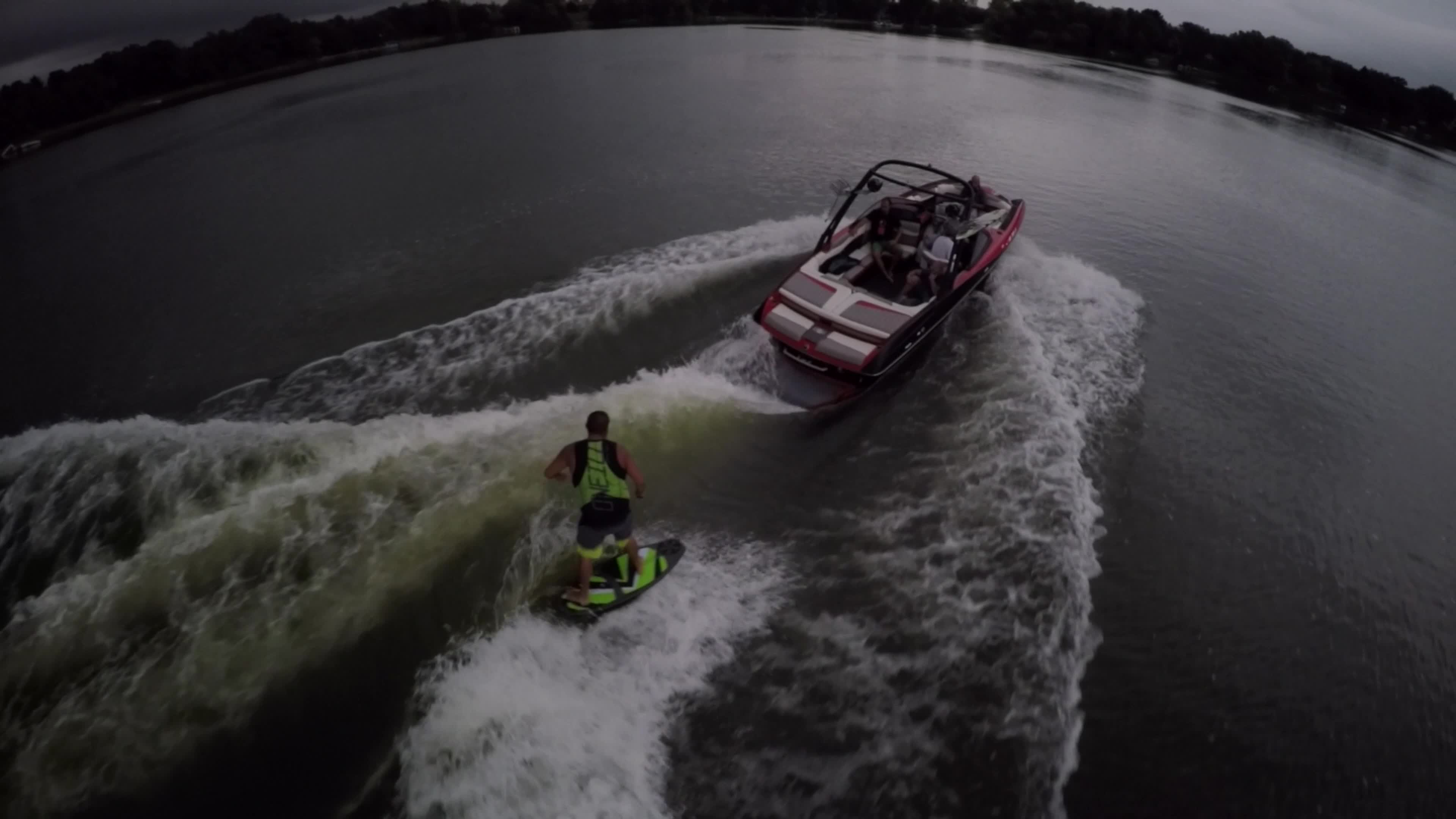 Aerial shot of a man wakeboard wake surfing behind a boat on a lake