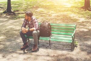hombre joven inconformista con mochila al lado de sentado en un banco de madera. foto
