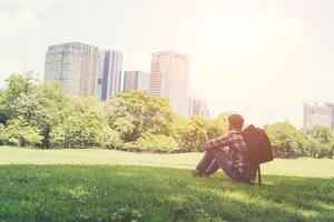 Rear view of relaxed young traveling man sitting on grass in the park. photo