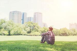 Rear view of relaxed young traveling man sitting on grass in the park. photo