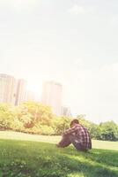 Rear view of relaxed young traveling man sitting on grass in the park. photo