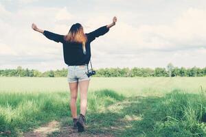 disfrutar de la parte posterior de la mujer joven que lleva la cámara retro en el campo de hierba. foto