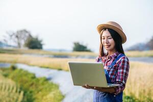 Smart woman farmer looking at barley field with laptop computer photo