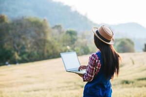 Smart woman farmer looking at barley field with laptop computer photo