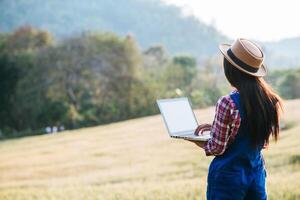 Smart woman farmer looking at barley field with laptop computer photo