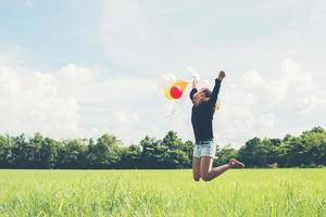 Hermosa mujer sosteniendo un globo sobre la hierba verde corriendo y saltando