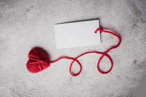 Red yarn heart shaped with white note card on the wall background photo