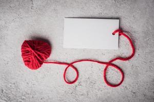 Red yarn heart shaped with white note card on the wall background photo