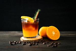 un vaso de café negro americano helado y una capa de jugo de naranja y limón decorado con romero y canela