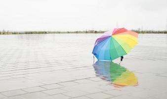 Rainbow colored umbrella lying in puddles on the wet street ground photo