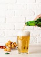 Beer pouring from bottle into glass, white brick wall background photo