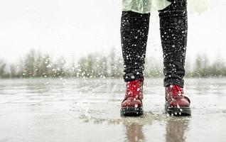 mujer jugando bajo la lluvia, saltando en charcos con salpicaduras foto