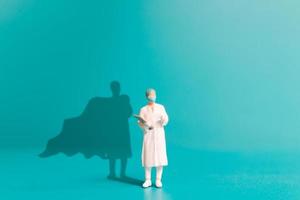 Médico de personas en miniatura con sombra de superhéroe en la pared. foto