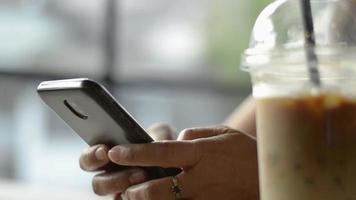 mujer charlando en las redes sociales en línea con el teléfono móvil bebiendo café con hielo. video