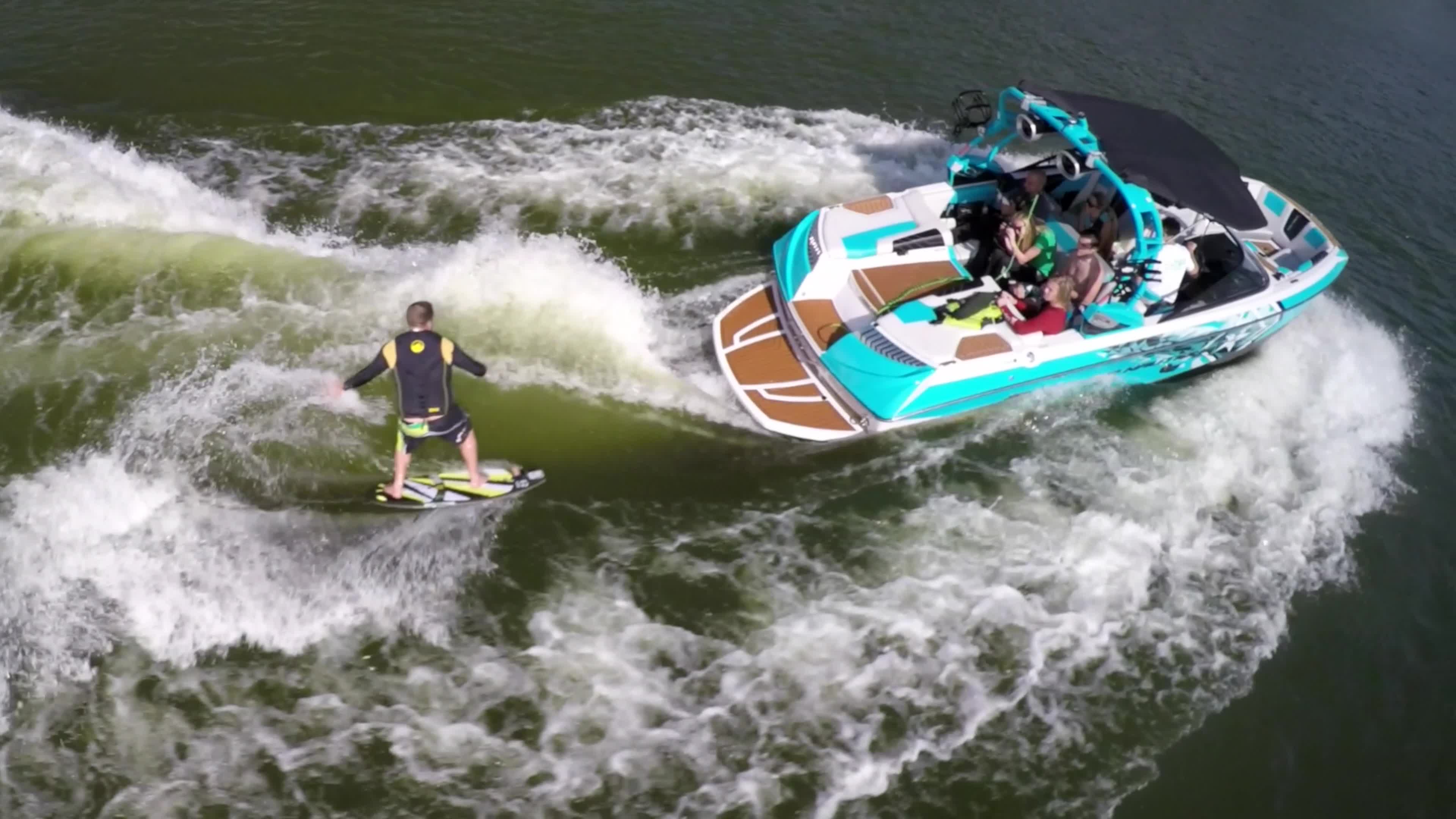 Aerial shot of a man wakeboard wake surfing behind a boat on a lake