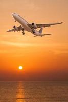 Commercial airplane flying over the sea at sunset photo