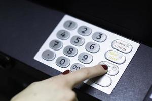 female hand dials a pin code at an ATM photo