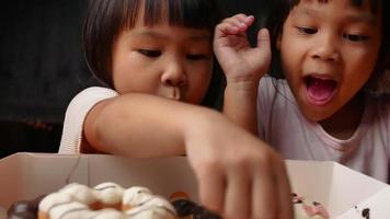 Happy adorable little girl pick up cute donuts from box. video