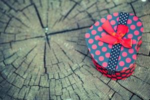 Caja de regalo en forma de corazón sobre tronco de madera foto