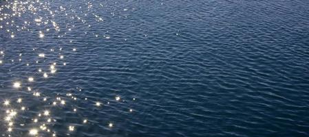 Blue sea water surface with ripples and sun reflections.