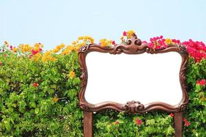 Sign with white background and wooden frame in front of garden photo