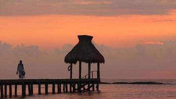 vrouw loopt langs dok tijdens zonsondergang in tropisch resort video