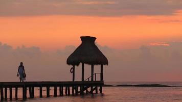 Mujer camina por el muelle durante la puesta de sol en el resort tropical video