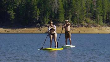 Couple on stand up paddle boards in lake video