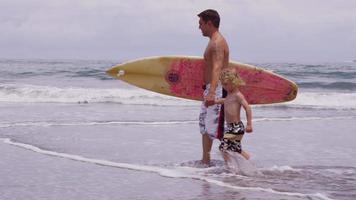 padre e figlio che camminano con la tavola da surf. video