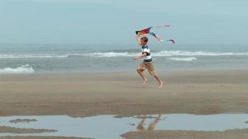 jongen loopt met vlieger op het strand, slow-motion video