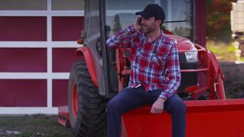 Farmer sits on tractor using cell phone video