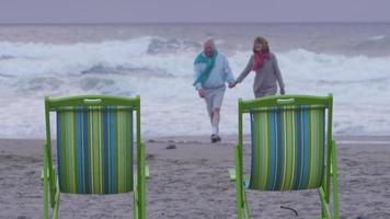 casal sênior caminhando na praia juntos video