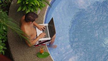 Man sitting on edge of hot tub using laptop computer. video