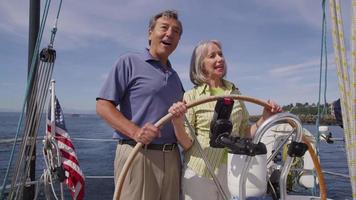 Senior couple behind the wheel of sailboat together. video