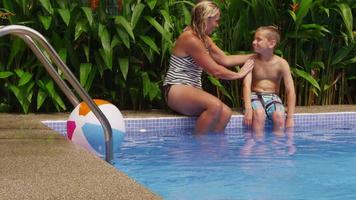 madre che mette la crema solare sul sole in piscina. video