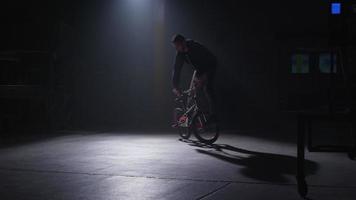 BMX rider doing tricks in dark warehouse. video