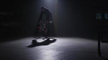 BMX rider doing tricks in dark warehouse. video