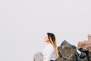 Una mujer joven y bonita de pelo largo con camisa blanca junto a las rocas foto