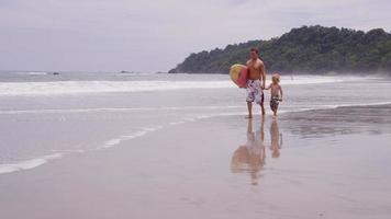 padre e figlio che camminano con la tavola da surf. video