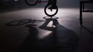 piloto de bmx haciendo trucos en el almacén oscuro. video